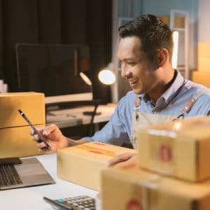 A shop owner looking at their phone surrounded by boxes